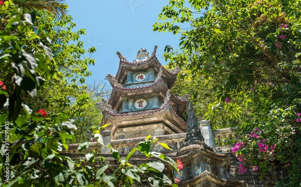 Obraz Buddhist pagoda hidden among trees and bushes. Pagoda against the blue sky surrounded by greenery. Vietnam.