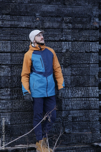 Fototapeta  Portrait of a young man with a beard in trendy colored winter clothes in front of a black wooden burned wall. Concept of fashion and style. Vertical photo.