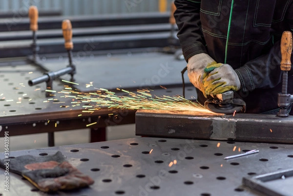 Fototapeta Worker grinding the junction between two sections of a metal square tube with circular grinder in a workshop