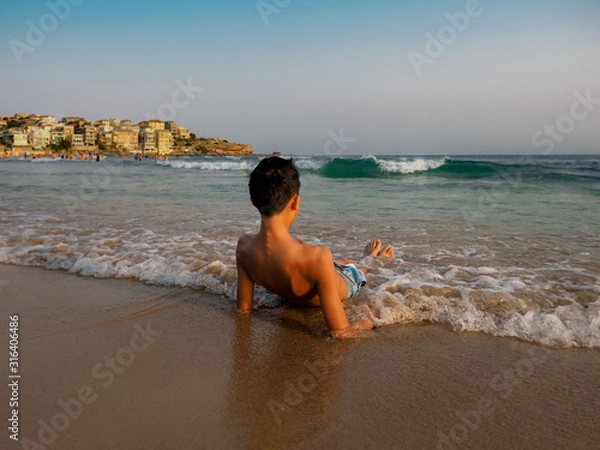 Fototapeta Closeup of an Asian boy relaxing on his back at the beach in the afternoon sunset.
