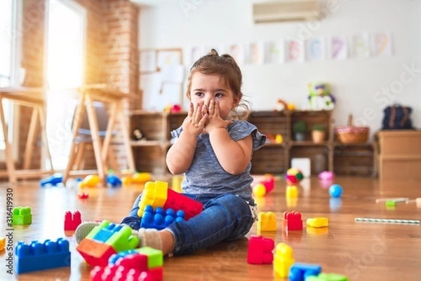 Fototapeta Beautiful toddler sitting on the floor playing with building blocks toys at kindergarten