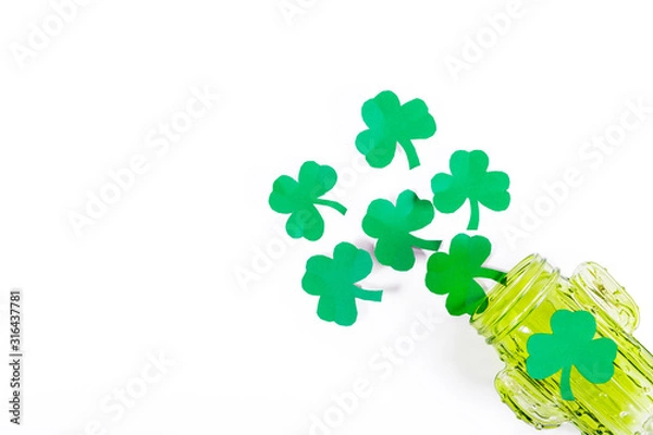 Fototapeta Green paper clover leaves spill out in the form of foam from a green glass
