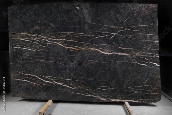 Fototapeta A slab of brown marble with light veins stands on a rack, called Port Laurent