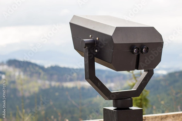 Fototapeta Touristic telescope look on top of mountains, close up metal binoculars on background viewpoint overlooking mountain