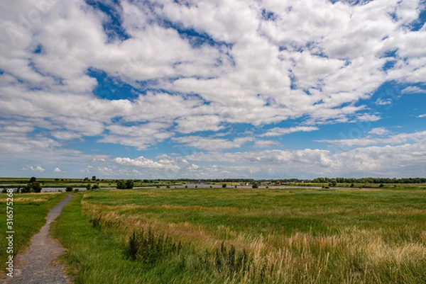 Obraz Scenic marsh landscape with view over a sewer with Marina in the background and wonderful white clouds in the blue sky, Greetsiel, Lower Saxony, North Germany