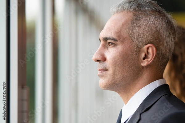Fototapeta Left Side Professional profile portrait of middle aged caucasian smart businessman while he looking something out of the windows which the hopeful and confident for the future. shot with copy space.