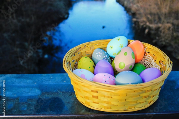 Obraz Bild von bunten Ostereiern in einem Korb und mir Fluss Hintergrund