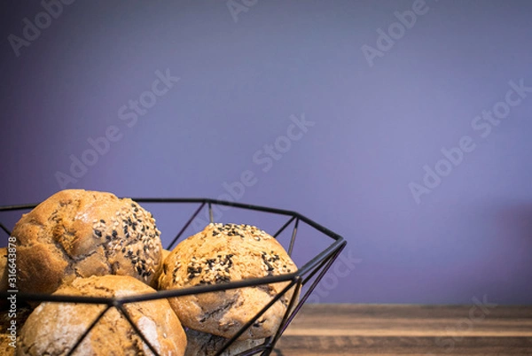 Fototapeta Selbst gebackene Brötchen in einer Schüssel auf einem Holzuntergrund mit freiem lilanen Hintergrund für eigenen Text 