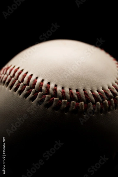 Fototapeta Close up of a leather baseball with red stitches. Low key, black background studio