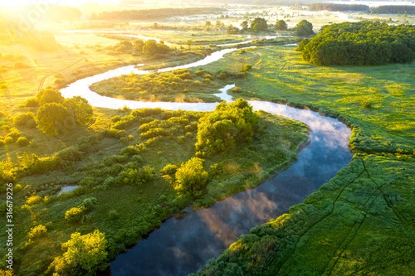 Fototapeta Widok z lotu ptaka na piękny krajobraz mglistej rzeki i zielonych pól. Wschód słońca nad rzeką latem