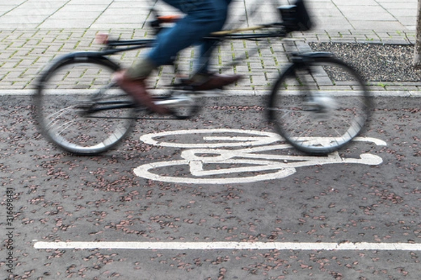 Fototapeta Painted cycle path bicycle sign on the ground with a rider passing.  Motion blurr on the bike and rider.