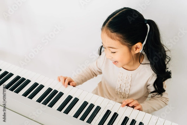 Obraz From above of happy smiling cute Asian girl playing piano enjoying time practicing music at home