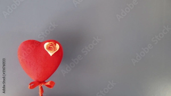 Fototapeta A red heart on a stick with a small red bow, decorated with a small red rose on a white background in the corner of a grey background. Saint Valentine's Day card concept. 