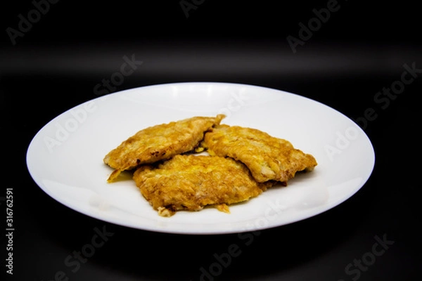 Fototapeta White plate with chops with meat on a black background. Fried meat in an egg on a plate. Three fried chops