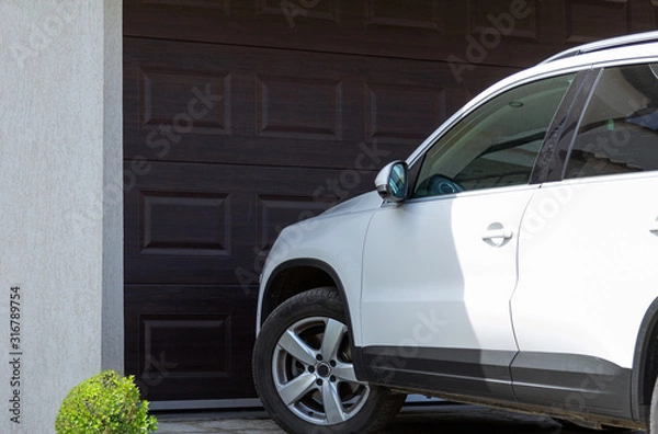 Fototapeta White car in front of modern house waiting to enter in the garage with large garage door