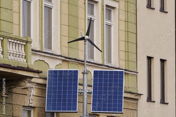 Fototapeta Street electricity by small windmill and solar panels in the city against buildings in daytime. Concept of renewable, eco or environmentally friendly and clean energy