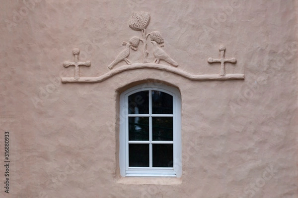 Fototapeta Fragment of the wall of an old church with a window decorated with a bas-relief in the form of two birds