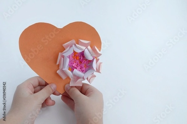 Obraz A heart made of orange paper with a flower, the child holds in his hands. With free space for text.
