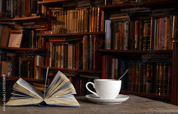 Obraz Open book. Nearby is a cup of coffee on a saucer and with a teaspoon. In the background shelves with books. Concept - coffee break, education, evening reading