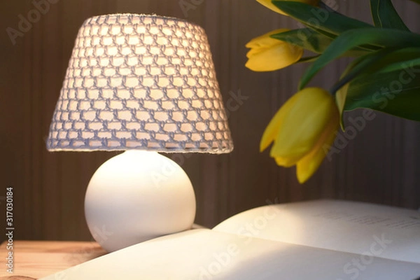 Fototapeta Still life. White table lamp with a knitted lampshade. Open book with blank sheets and tulips stand on the table. Atmosphere