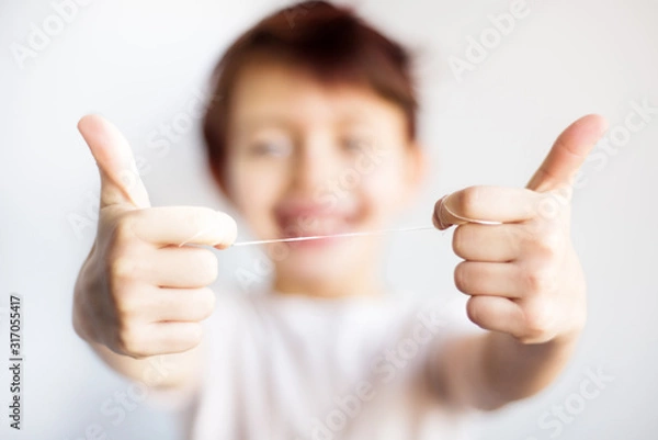 Obraz Closeup of dental floss in child hands. Happy child in white t-shirt out of focus hold floss for teeth in two hands. Dental and health care. Correct dental care from childhood save teeth for life.