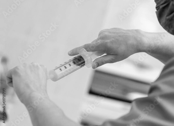 Fototapeta Close-up of the hands of an assistant surgeon with a syringe that is collecting fluid from an ampoule. b / w