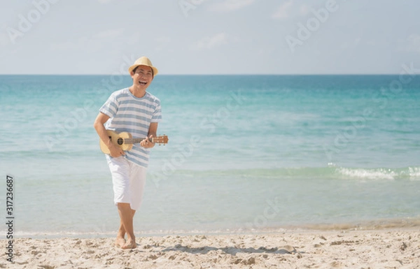 Fototapeta Asian man playing a ukulele and singing with enjoy on a tropical beach, Live life happily on holidays.