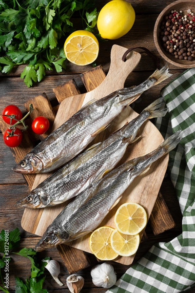 Fototapeta Smoked or dried smelt fish on a wooden Board on a brown wooden table. Top view with space for text	