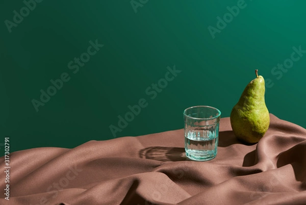 Fototapeta classic still life with pear and water in glass on table with brown tablecloth isolated on green