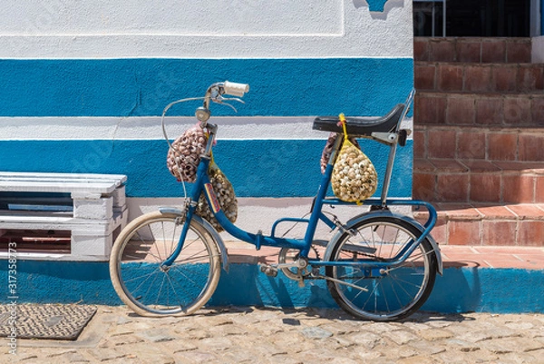 Fototapeta Bicycle caring snails in meshes in front of a blue and white house in Algarve, Portugal