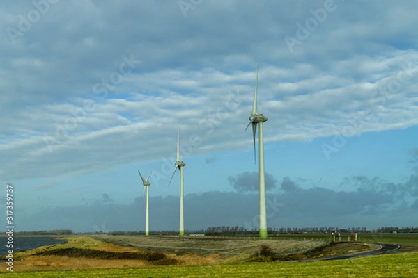 Fototapeta three Dutch windmills in a row for creating windenergy, next to the water in Zeeland, the Netherlands