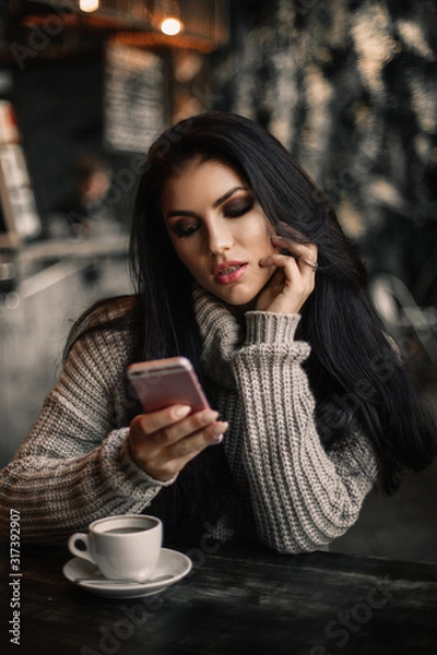 Fototapeta Woman using phone and drinking coffee in a cafe.