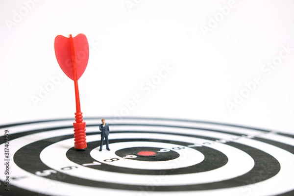 Fototapeta Business strategy conceptual photo - Miniature businessman with red arrow on a dartboard