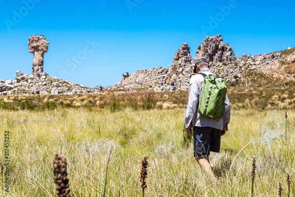 Fototapeta Man hiking to the rock formation Maltese Cross - a popular destination in the Cederberg, with fynbos vegetation, South Africa