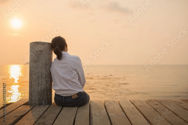 Fototapeta Beautiful woman sitting Alone with loneliness At the wooden bridge by the sea During sunset