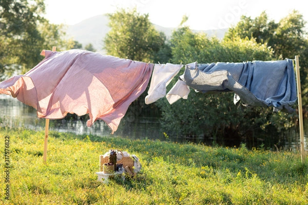 Fototapeta Pink and blue bedding sheet on forest background under the bright warm sun. Clean bed sheet hanging on clothesline at backyard. Hygiene sleeping ware concept.