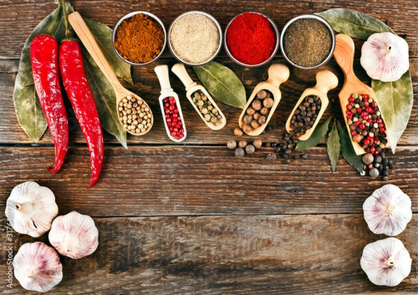 Fototapeta Red hot chili pepper, different pepper in ceramic cups, peppercorn in scoops, bay leaves and garlic on wooden background. Text space. Top view.