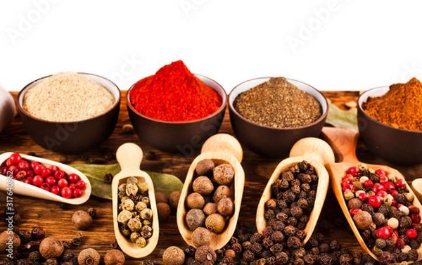 Fototapeta Different peppers in ceramic cups and peppercorns in wooden scoops on wooden background.