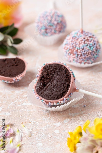 Fototapeta  Sectional view Round chocolate cake pops with pink and yellow spring flowers on a marble background. Image with a vertical orientation.