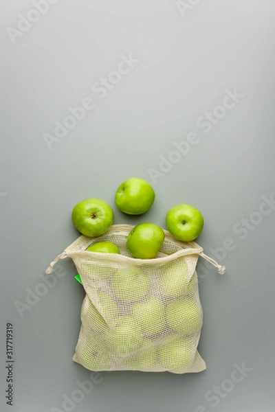 Fototapeta Green apples in a reusable cotton bag on a gray background.