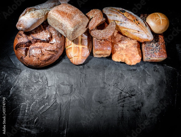 Fototapeta Assortment of fresh baked bread on dark background. White and rye bread, buns with copy place