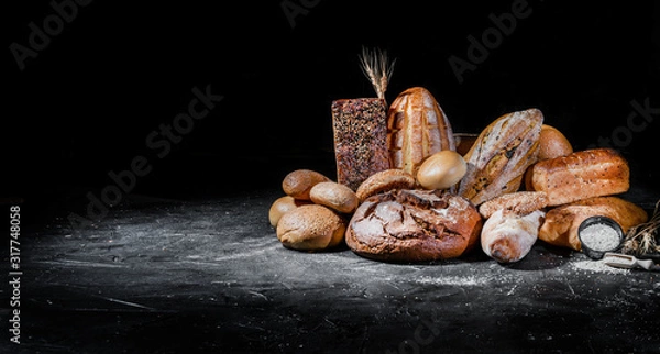 Fototapeta Assortment of fresh baked bread on dark background. White and rye bread, buns with copy place