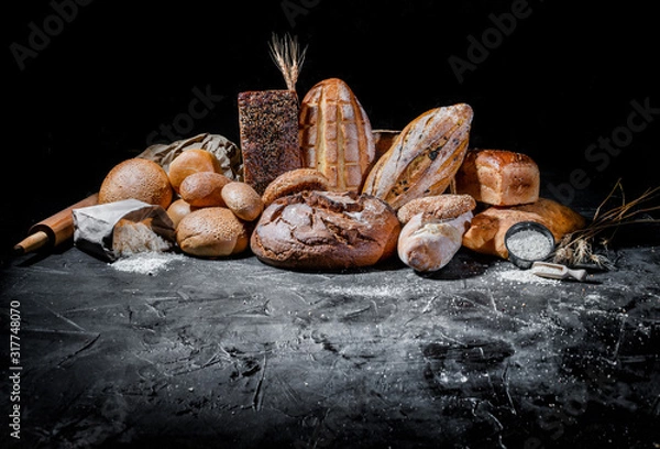 Fototapeta Assortment of fresh baked bread on dark background. White and rye bread, buns with copy place