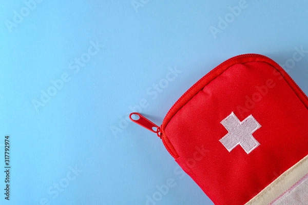 Fototapeta Closed red travel first aid kit pouch on the bright blue background. Photo with a copy space