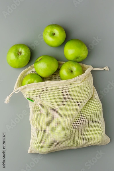 Fototapeta Green apples in a reusable cotton bag on a gray background.