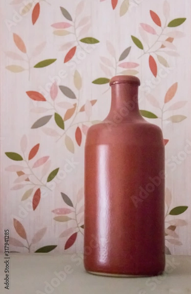 Obraz Clay vase in the form of a bottle standing on a background depicting plants. Background