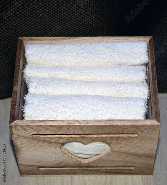 Fototapeta Wooden box for white towels. Face towel. Skin care. White towels in a wooden box on a brown background.