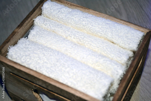 Obraz Wooden box for white towels. Face towel. Skin care. White towels in a wooden box on a brown background.