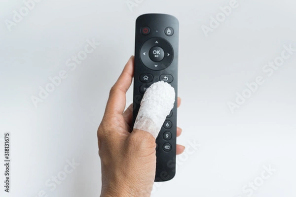 Fototapeta The thumb was wrapped in a white bandage due to an accident touch black remote control on white background