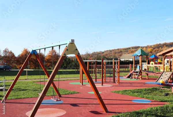 Fototapeta Wisniowa, Poland - oct 12 2018: Children's playground in the park amidst greenery. Multicolored swings and buildings for children from metal and wood. Place of play of the younger generation